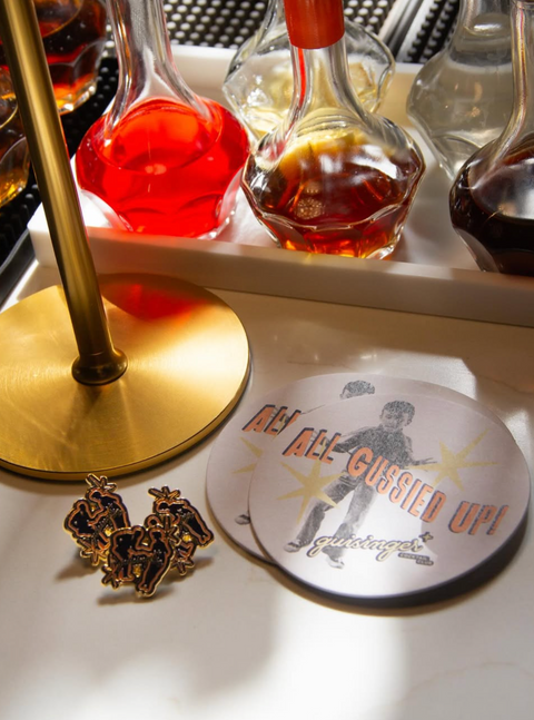Coasters with custom graphic design on bar next to custom die-cut enamel pins.